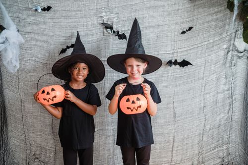 Free Two smiling girls in witch costumes with Jack-O'-Lanterns celebrate Halloween indoors. Stock Photo