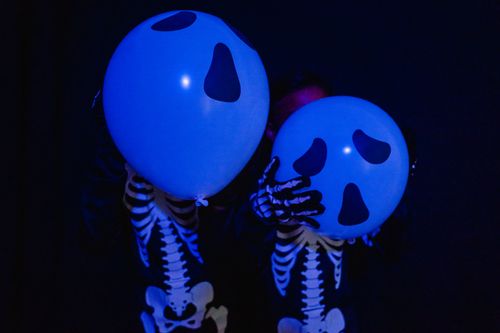 Free Two children wearing skeleton costumes holding spooky blue balloons in a dark setting. Stock Photo