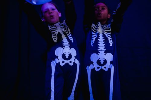 Free Two kids dressed in skeleton costumes raise their arms in spooky fun at a Halloween party. Stock Photo