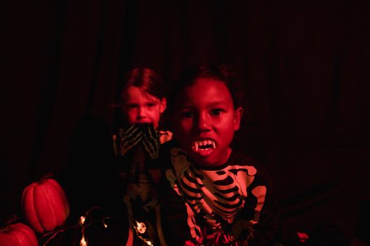 Two kids in skeleton costumes with vampire teeth and pumpkins, perfect for Halloween-themed visuals.