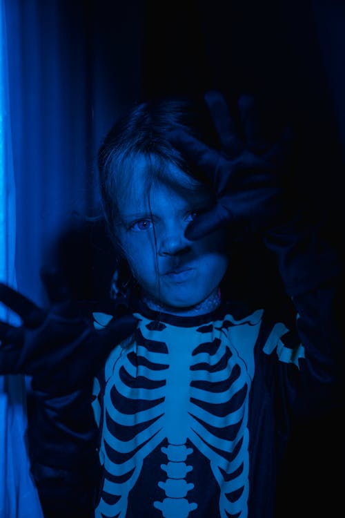 Young girl in skeleton costume in darkness under blue light