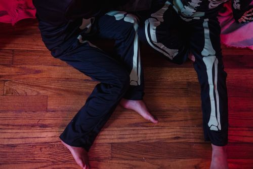 Free Two children dressed in skeleton costumes play on a wooden floor indoors, capturing a spooky and fun atmosphere. Stock Photo
