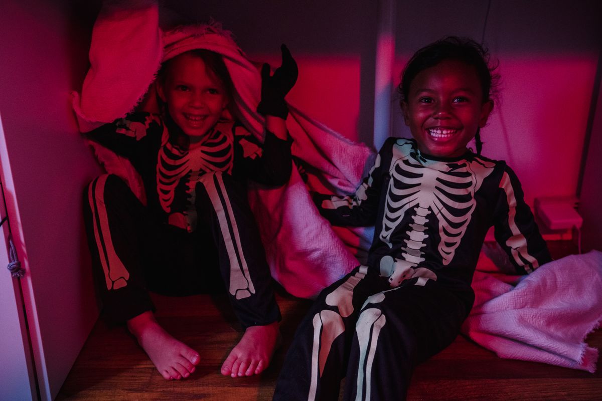 Two children laughing in skeleton costumes at Halloween.