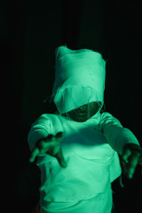 Free Child in mummy costume with arms outstretched under eerie green lighting, perfect for Halloween themes. Stock Photo
