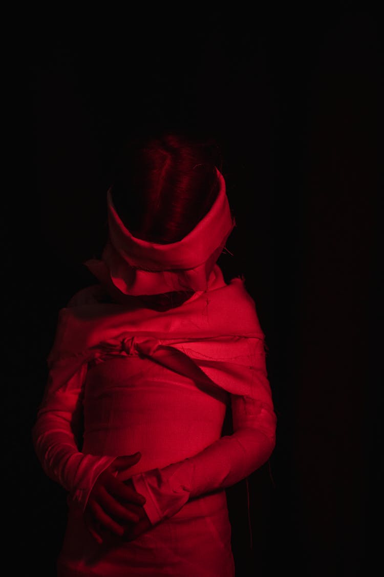 Kid Wearing Mummy Costume And Standing In Red-lighted Room