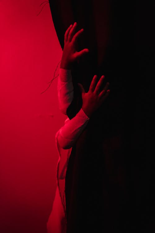 Two hands on black curtain in red-lighted room