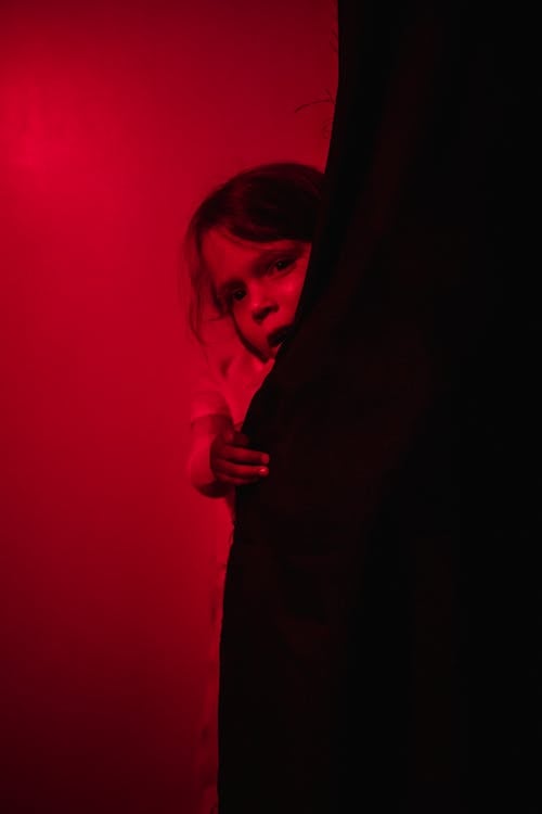 Scared girl behind black curtain in red-lighted room