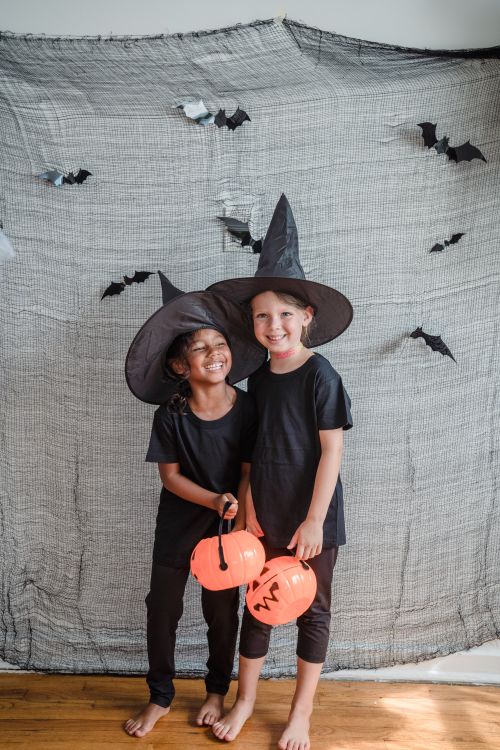 Free Two children in witch costumes with pumpkin buckets celebrating Halloween indoors. Stock Photo