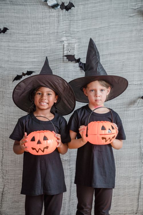Free Two girls in witch costumes holding pumpkin buckets, celebrating Halloween indoors. Stock Photo