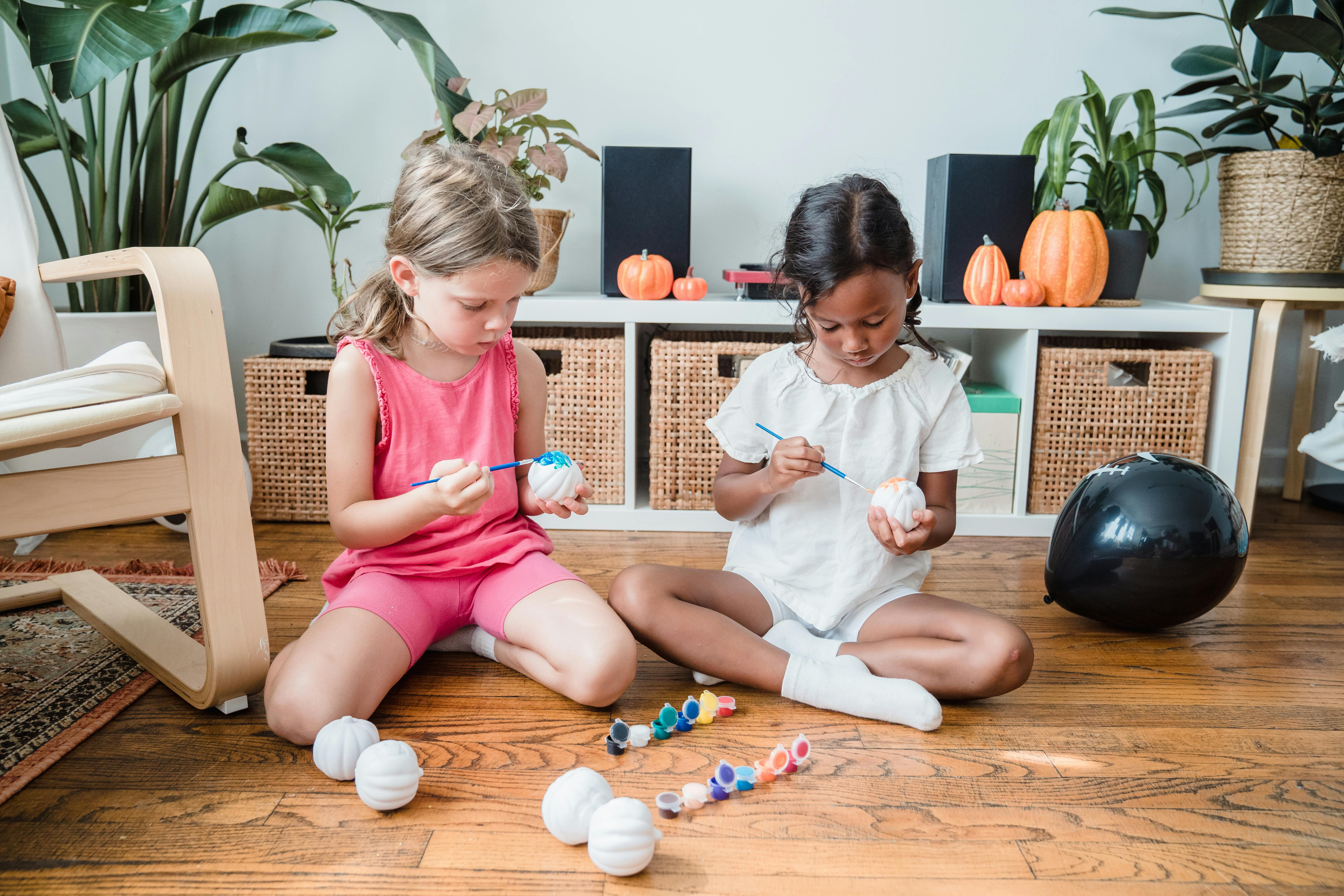 Two girls sitting on wooden floor in room and painting