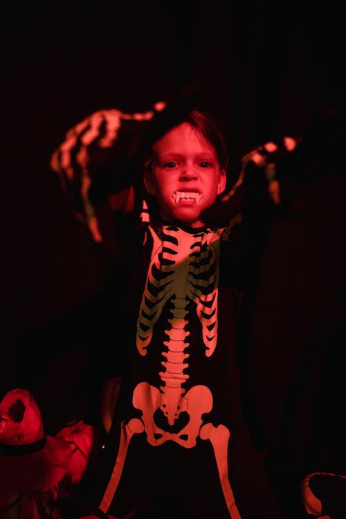 Kid wearing skeleton costume and vampire teeth standing in spooky posture