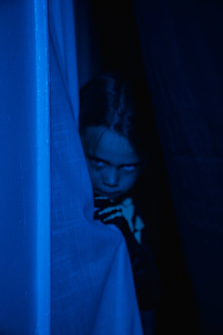 Child Hiding Behind The Curtain In A Blue Light