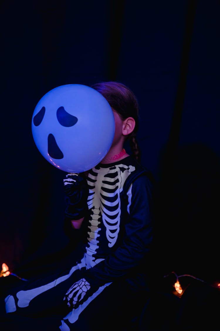 Girl Sitting In Skeleton Costume With Balloon Imitating Her Head