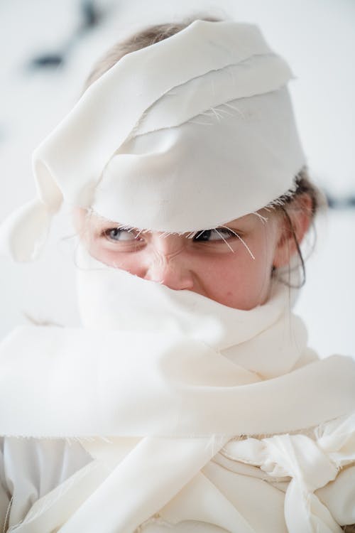 Girl wrapped with strips of white fabric pretending scary mummy