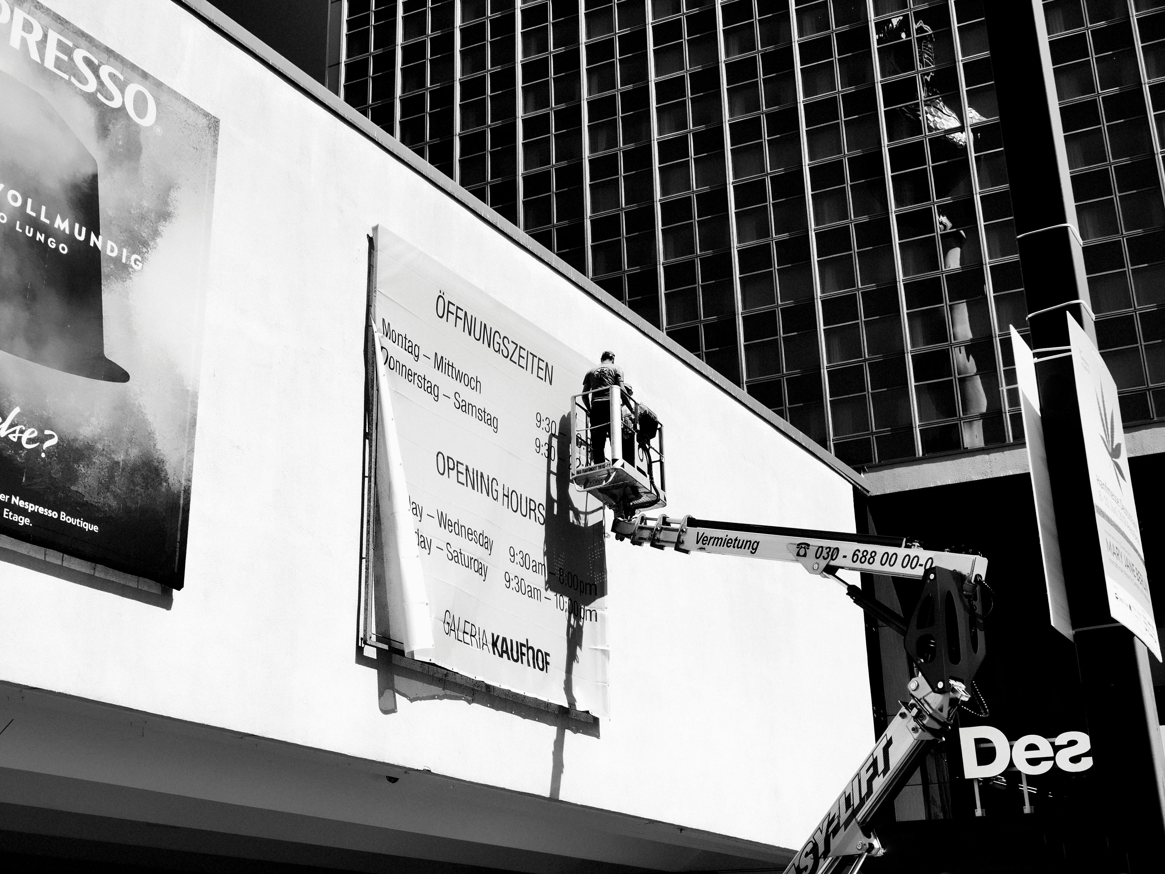Monochrome shot of a worker on lift adjusting a billboard outside building.