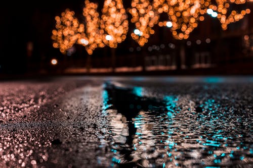 Selective Focus Photography of Asphalt Road With Water Droplets Near City Lights during Nighttime