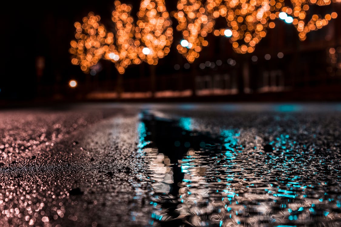 Selective Focus Photography of Asphalt Road With Water Droplets Near City Lights during Nighttime