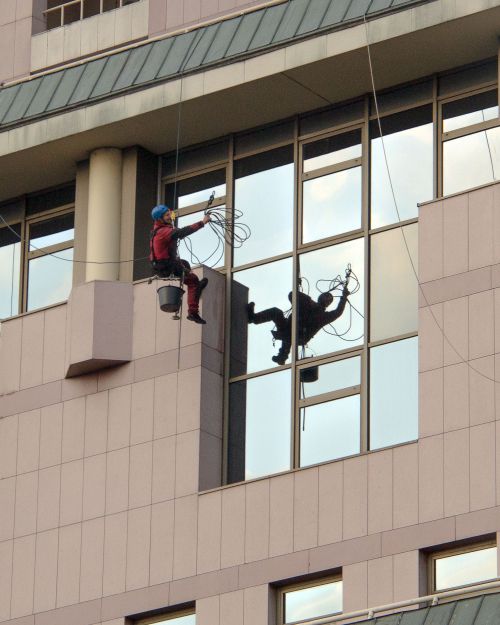 Free Two professional window cleaners working on a skyscraper, ensuring safety with harnesses. Stock Photo