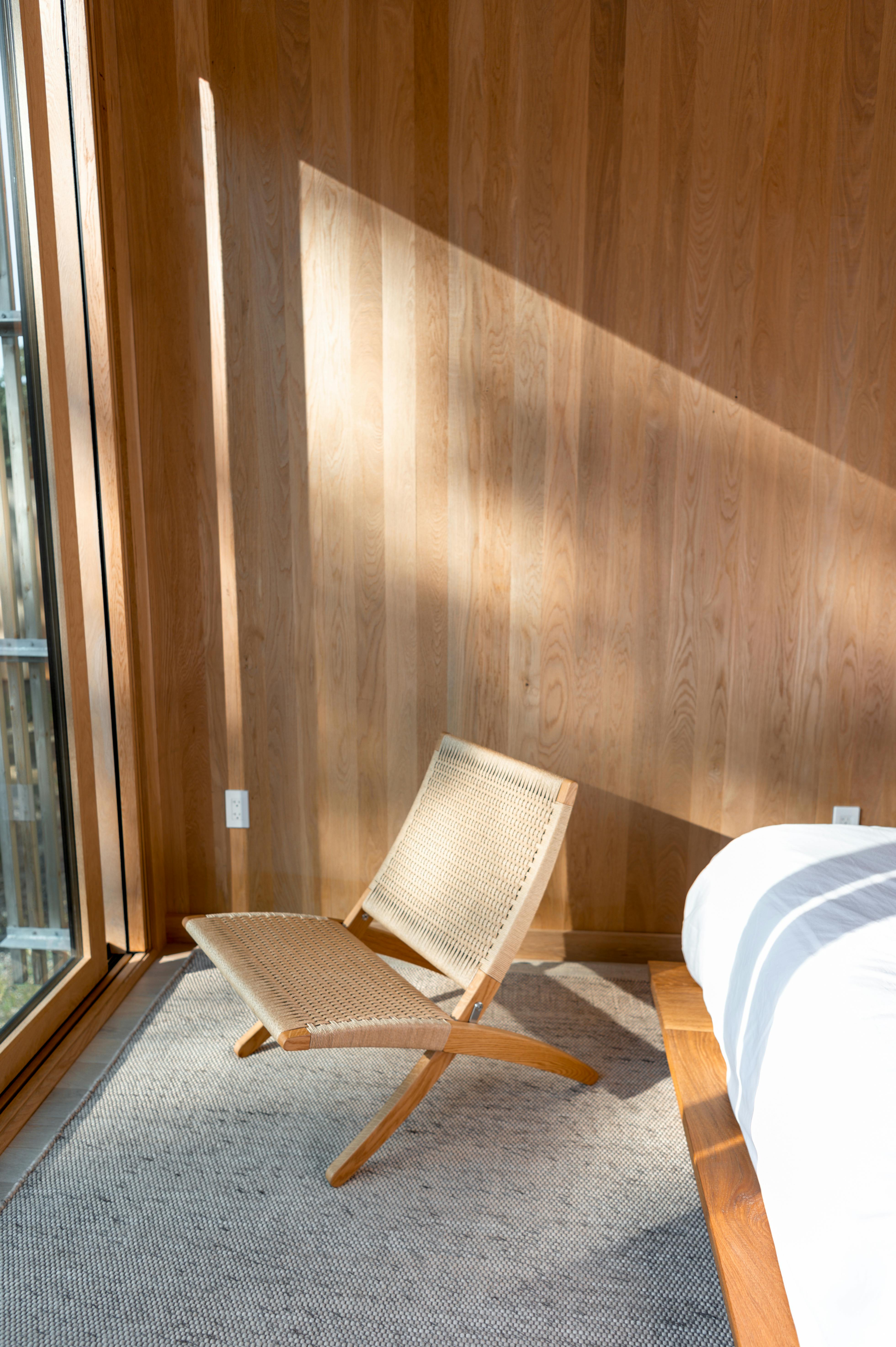 Bright and tranquil bedroom featuring a rattan chair and wooden elements, epitomizing minimalist interior design.