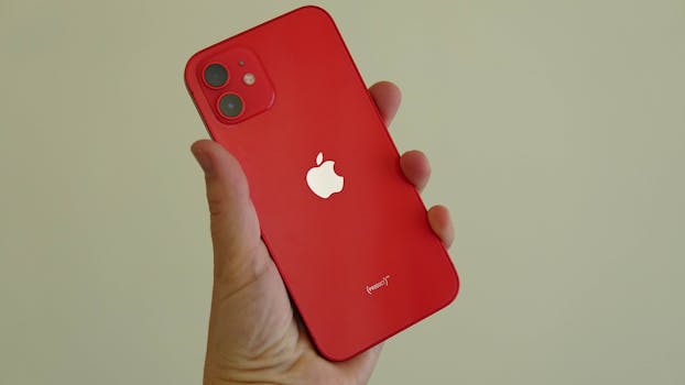 Close-up of a hand holding a red smartphone against a neutral background.