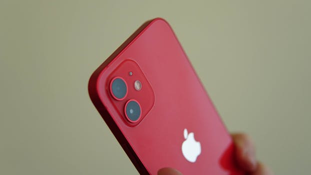 Red smartphone with dual cameras held against a neutral background, showcasing modern design.