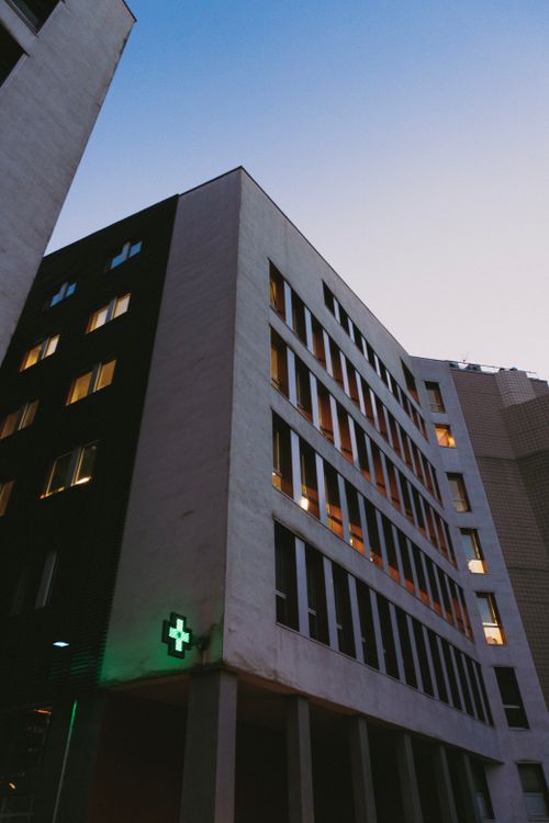 Free Low angle view of a modern hospital building with a green cross at dusk. Stock Photo