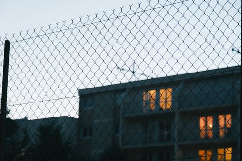 Free A city building with glowing windows viewed through a wire mesh fence at dusk. Stock Photo