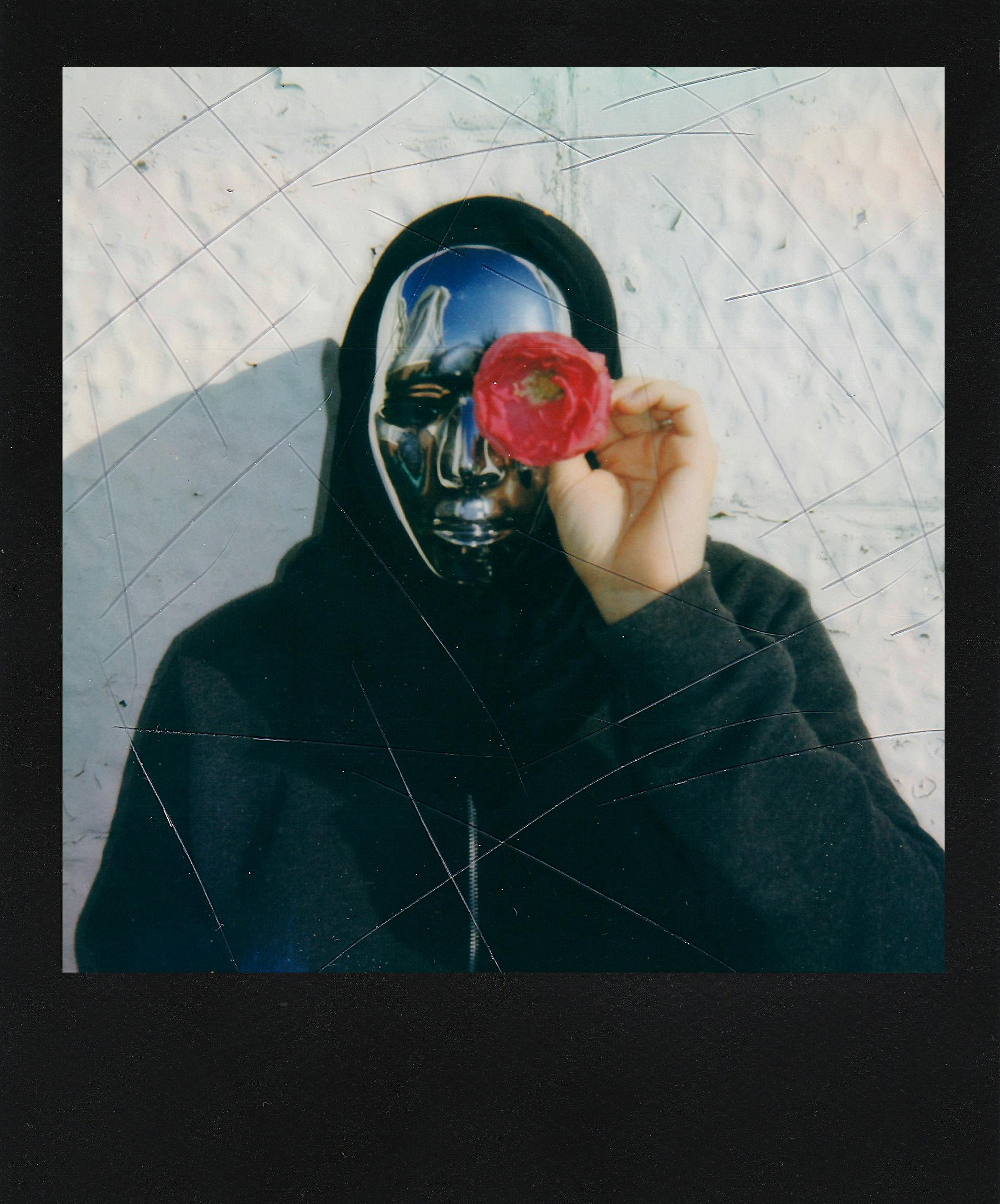 A person wearing a metallic mask holding a red rose, evoking mystery and intrigue.