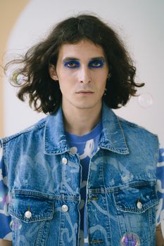 Artistic portrait of a man with bold make-up and denim vest, capturing unique style.