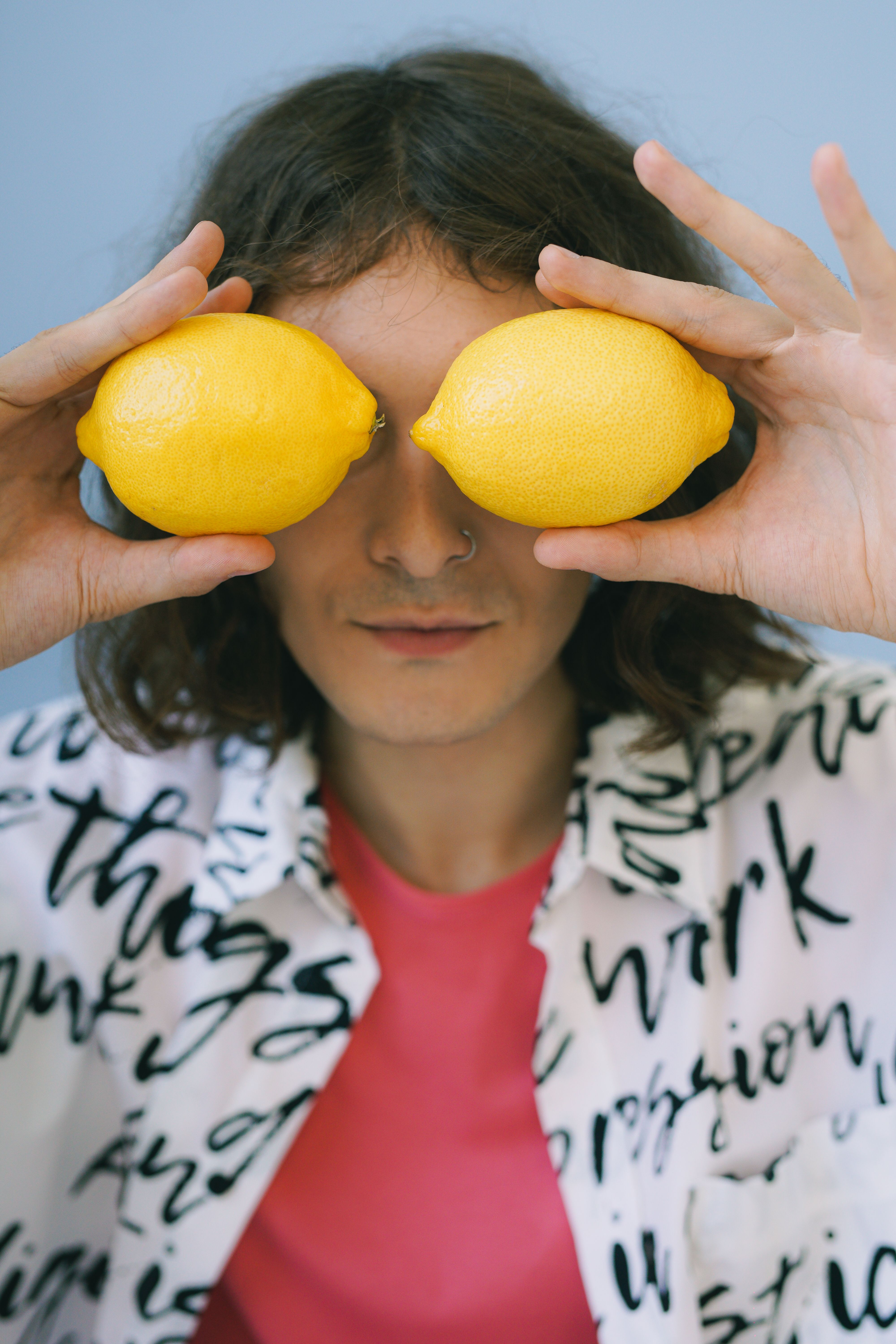Man holding lemons to cover eyes in a stylish studio portrait.