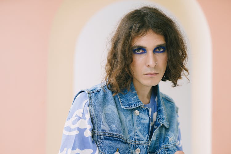 Man With Long Hair And Makeup Standing Under Arcade