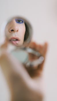 Reflective image of a person with makeup in a handheld mirror, showcasing personal style.
