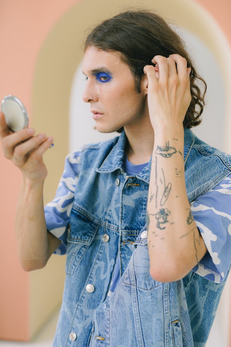 Man In Blue Eyeshadow Checking Himself In Pocket Mirror