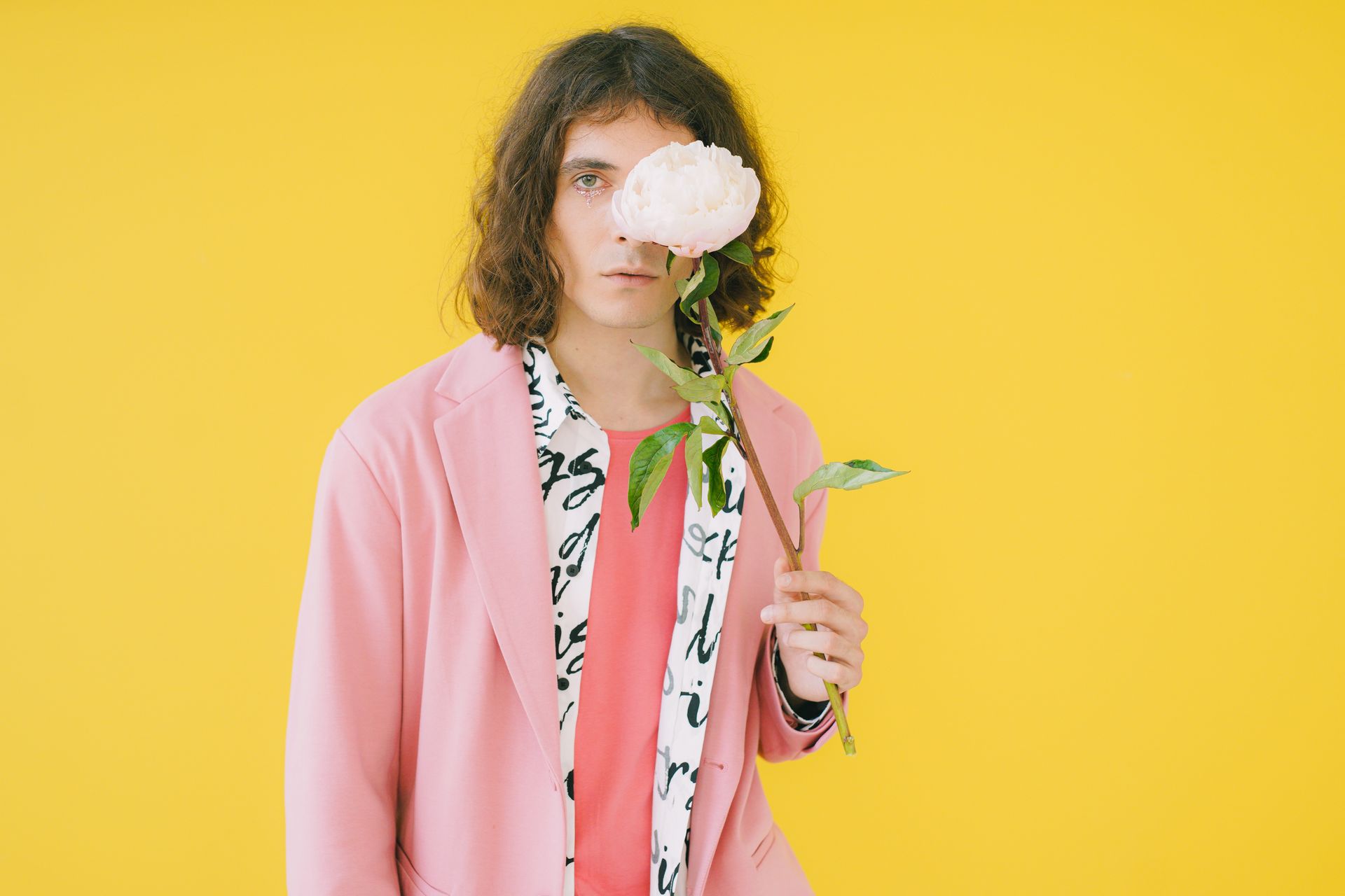 Fashionable portrait of a man holding a pink peony against a vibrant yellow background.