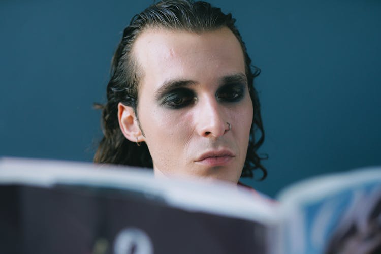 Portrait Of Man With Slicked Back Hair And Eyeshadow Reading Magazine