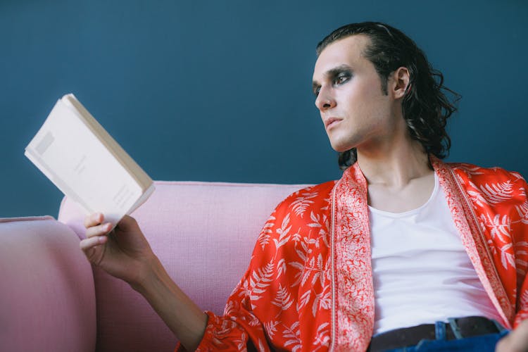 Man In Red Robe Sitting On Couch Reading Book