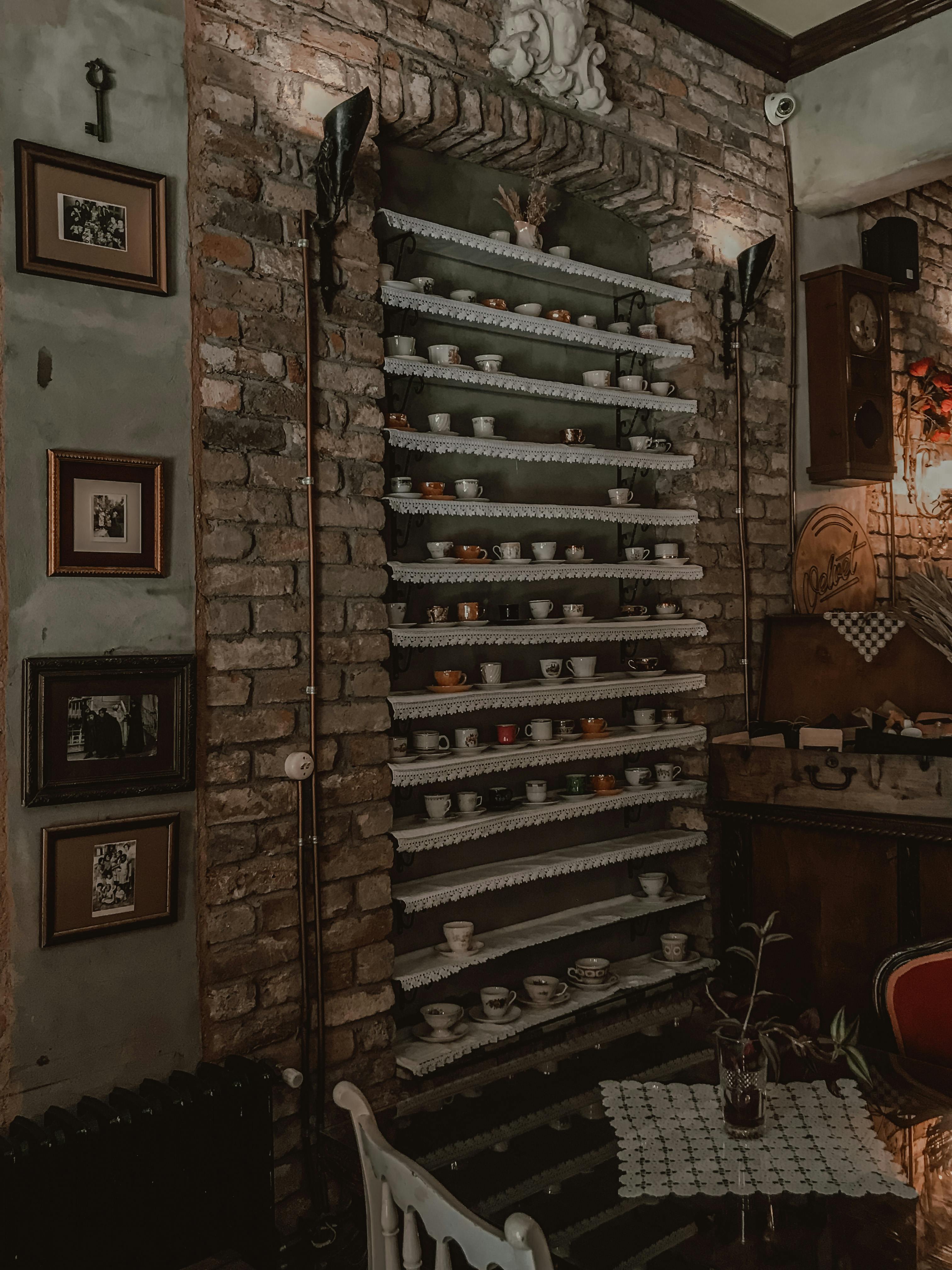 Free Cozy vintage interior with brick wall and ornate shelves displaying assorted teacups for a rustic charm. Stock Photo