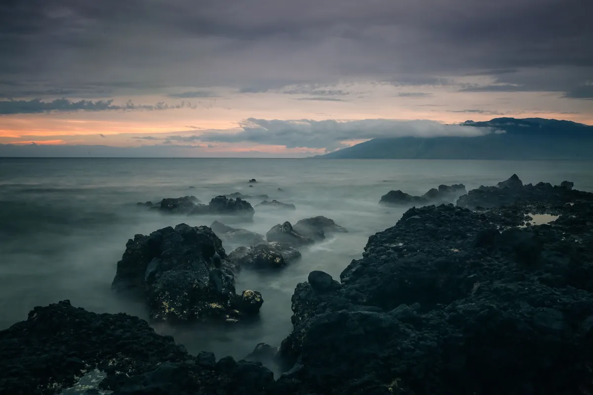 Golden Hawaii sunset glowing over the ocean and dark lava rocks