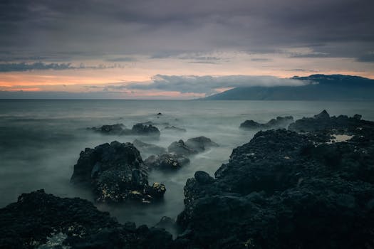 Captivating long exposure of rocky seascape at sunset in Kula, Hawaii, with mist and clouds.
