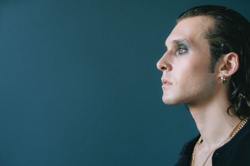 Free Portrait of a man with dramatic makeup and long hair, gazing into distance against a blue background. Stock Photo