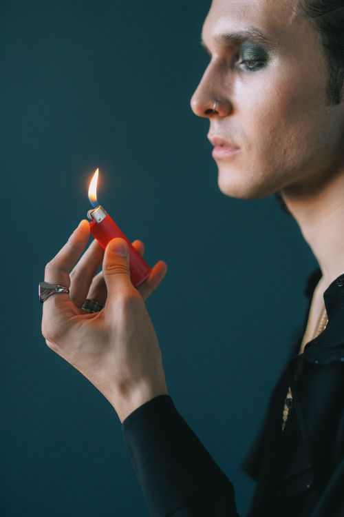 Free A young man looks contemplatively at a lit lighter in his hand, against a moody background. Stock Photo