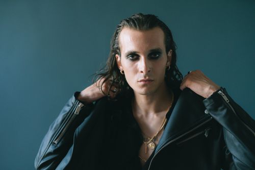 Free A fashionable man with striking eye makeup in a black leather jacket poses confidently. Stock Photo
