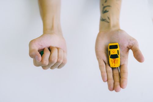 Free Top view of tattooed hands holding a yellow toy car on a white background, depicting creativity and childhood nostalgia. Stock Photo