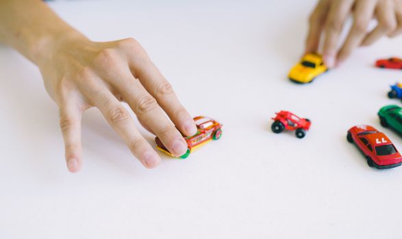 Close-up of adult hands playing with colorful toy cars on a white surface.