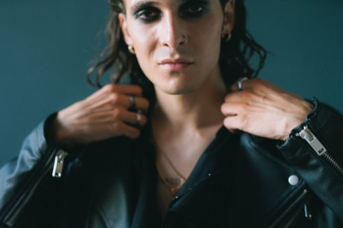 Free Portrait of a man in a black leather jacket showing edgy eye makeup, posing indoors. Stock Photo