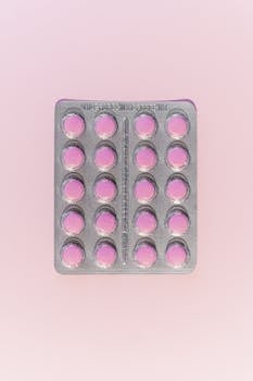 Close-up of blister pack with pink pills on a pastel background. Flat lay view.
