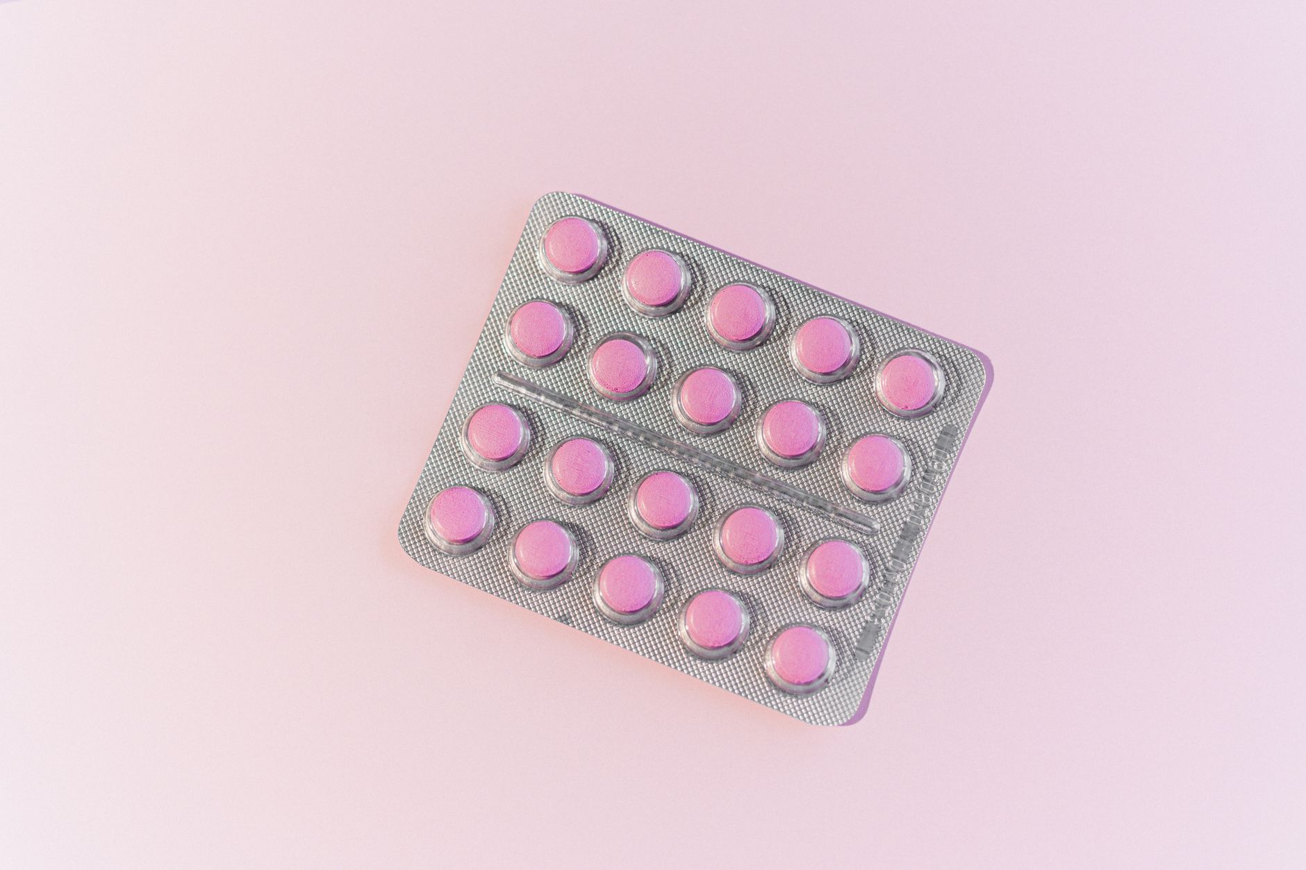 Top view of pink tablets in a blister pack on a light pink background.