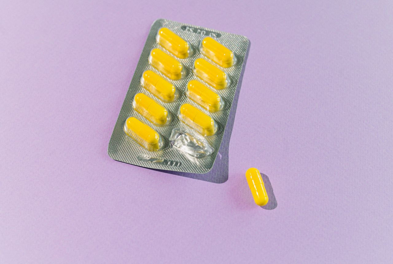 a blister pack of yellow capsules with one pill on a purple backdrop