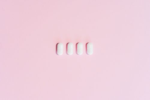 White capsules aligned on a soft pink surface — photo by SHVETS production on Pexels