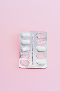 Close-up of a blister pack with white pills on a pastel pink background, perfect for healthcare themes.